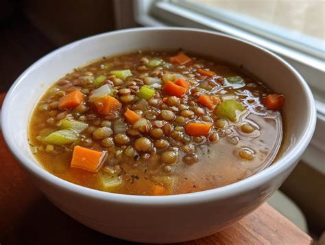 Plato de sopa de lentejas caliente en un bol, con hierbas frescas y humeante