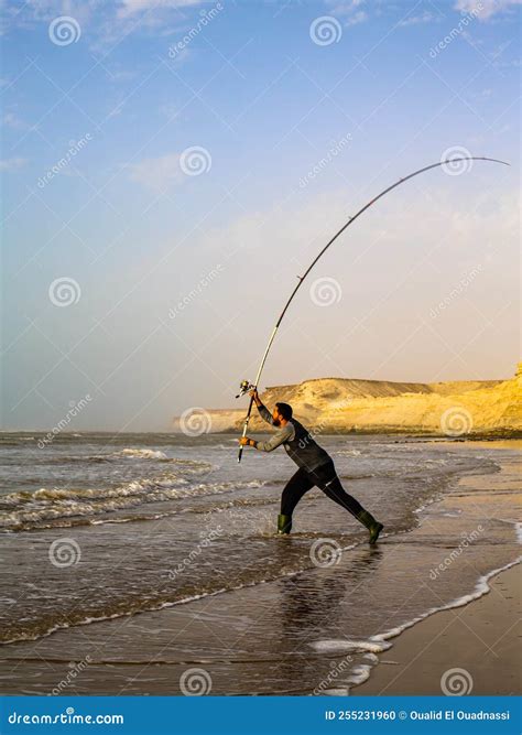 Un pescador lanzando su caña en un río caudaloso con montañas nevadas al fondo.