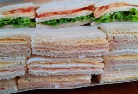 Plato de sándwiches de jamón variados, decorados con hierbas frescas.