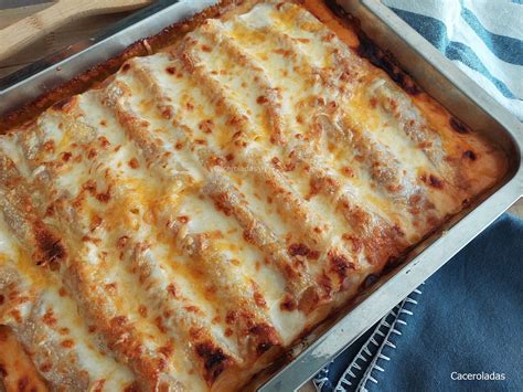 Fuente de horno con canelones cubiertos de bechamel y queso, listos para hornear.