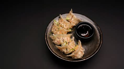 Persona disfrutando de una bandeja de gyozas al vapor con salsa de soya y arrollados primavera crujientes en un ambiente de restaurante moderno