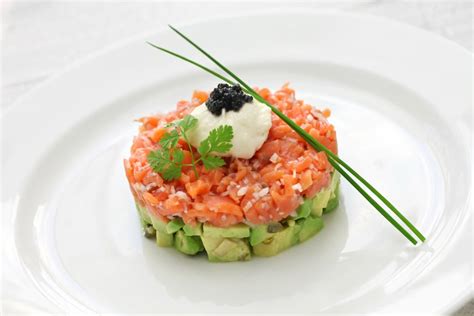 Presentación elegante de un tartar de salmón y espinacas en un plato.