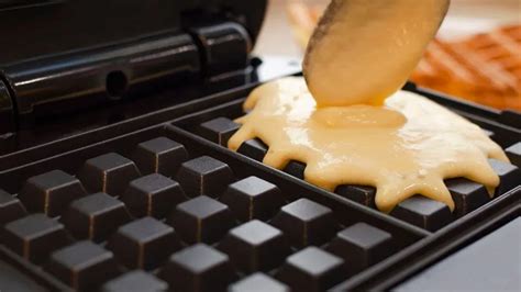 Foto de una wafflera moderna en uso, mostrando la masa vertiéndose en los moldes.