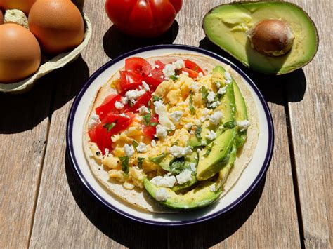 Plato de huevos revueltos con tocino, aguacate y vegetales frescos sobre un fondo rústico