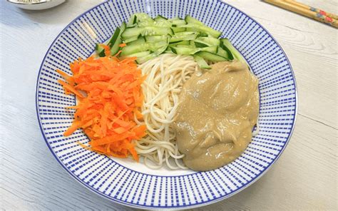 Primer plano de un bol con fideos taiwaneses májiàng miàn, decorados con juliana de pepino y zanahoria.
