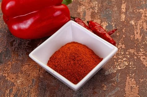 Pimentón en polvo rojo vibrante en un cuenco de madera junto a pimientos secos