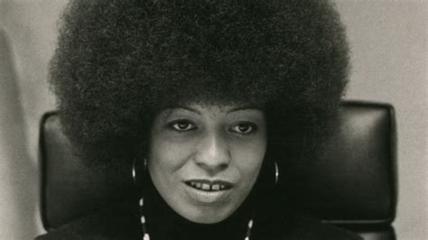 Retrato de Angela Davis en un evento de activismo, posiblemente en una conferencia o manifestación, con una expresión de determinación.