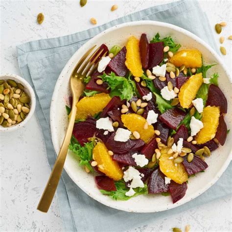 Fotografía cenital de una ensalada fresca con gajos de naranja, frutos secos y un cuenco pequeño con la vinagreta de miel y naranja al lado