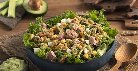 Foto de una elegante copa de cristal servida con ensalada de atún multicolor, decorada con láminas de aguacate y una rodaja de limón en el borde