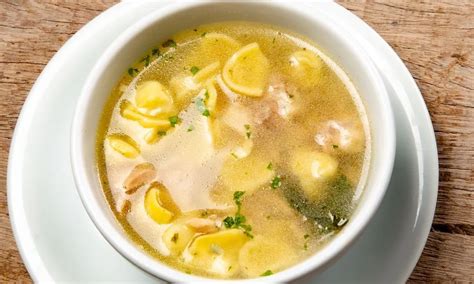 Tazón de sopa de capeletti con chorizo, con ingredientes frescos al lado