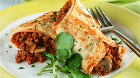 Fotografía gourmet de crepes rellenos de carne de jaiba y alcachofas, decorados con cebollino y una salsa cremosa al vermut