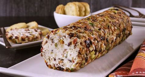 Rollo de queso crema finalizado, cubierto de sésamo y decorado con ciboulette, listo para cortar.