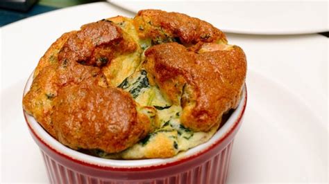 Fotografía profesional de un soufflé de pollo con espinacas recién salido del horno, servido en un plato de greda artesanal.