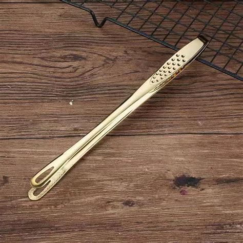 Imagen de unas pinzas de barbacoa largas y robustas junto a una parrilla.