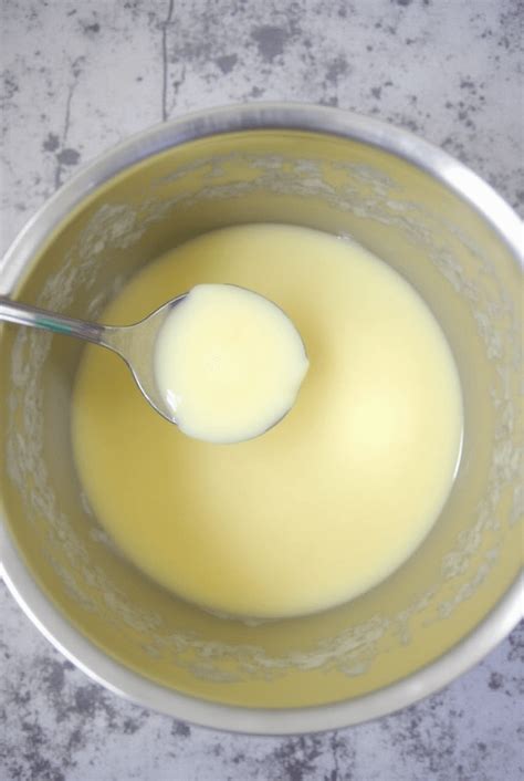 Tazón con mantequilla batida y leche condensada siendo añadida gradualmente.