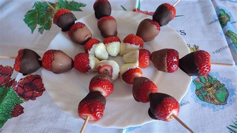 Brochetas de fresas con chocolate cubriendo solo una parte, adornadas con trozos de nueces y almendras