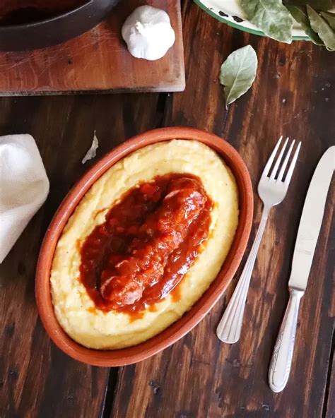 Plato servido de chorizos a la pomarola con una guarnición de puré, mostrando la textura de la salsa de tomate y vegetales