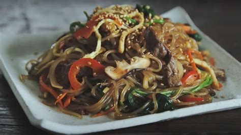 Fotografía gastronómica de un plato de Japchae coreano elaborado con fideos de almidón de camote y vegetales salteados.