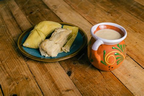 Mesa con una amplia variedad de tamales mexicanos y atole humeante, mostrando diferentes envolturas y rellenos.