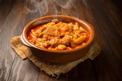 Fotografía detallada de un plato de picante de mondongo servido con guarniciones tradicionales en una vajilla de barro.