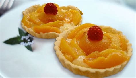 Fotografía profesional de una tartaleta de durazno decorada con láminas de fruta fresca y crema pastelera.