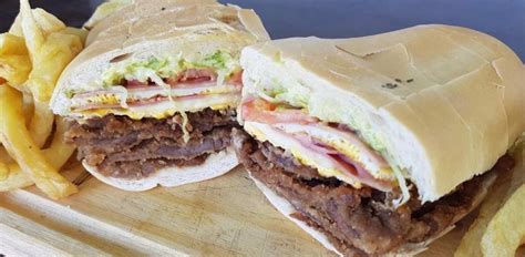 Fotografía profesional de un sándwich de milanesa tucumano completo, destacando la jugosidad de la carne y el pan fresco.