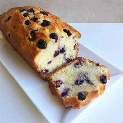 Foto de un budín de yogur y arándanos cortado, mostrando su interior húmedo y los frutos azules.