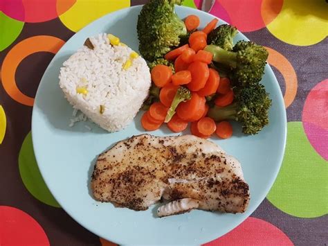 Plato de pescado al horno servido con arroz blanco y verduras.