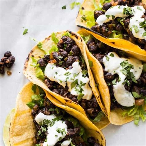 Fotografía de tacos de frijoles negros y camote con aderezos frescos.