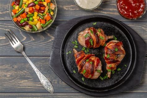 Foto de piernas de pollo envueltas en tocino ya cocidas y servidas con verduras asadas
