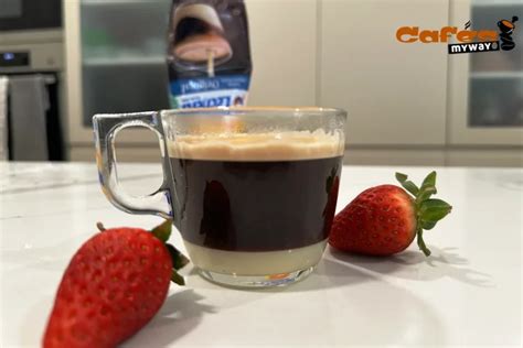Vertiendo café espresso lentamente sobre leche condensada en un vaso de cristal