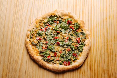 Fotografía cenital de una pizza artesanal con base verde, coronada con espinacas frescas y una generosa capa de queso fundido.