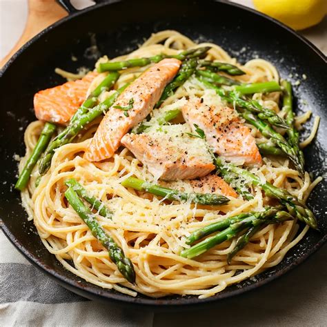 Plato de pasta con espárragos frescos, láminas de salmón ahumado y una cremosa salsa de limón, servido con elegancia.