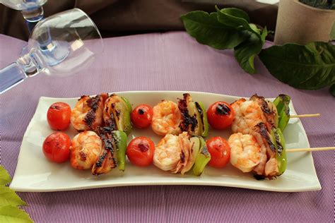 Plato de brochetas de langostinos con una ensalada fresca y una salsa.