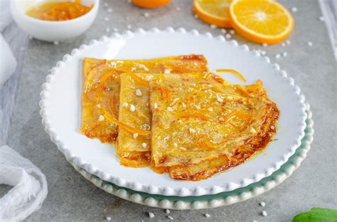 Fotografía de crepes Suzette flameadas, con una copa de vino naranjo al lado.